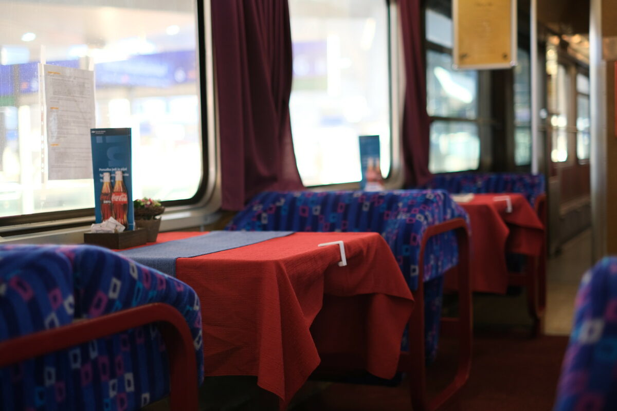 A picture of the interior of the SZ dining car. its colorful seat coverings, and table cloths. The colors blue and red are dominating. There are also dark red curtains. Everthing looks more or less vintage.