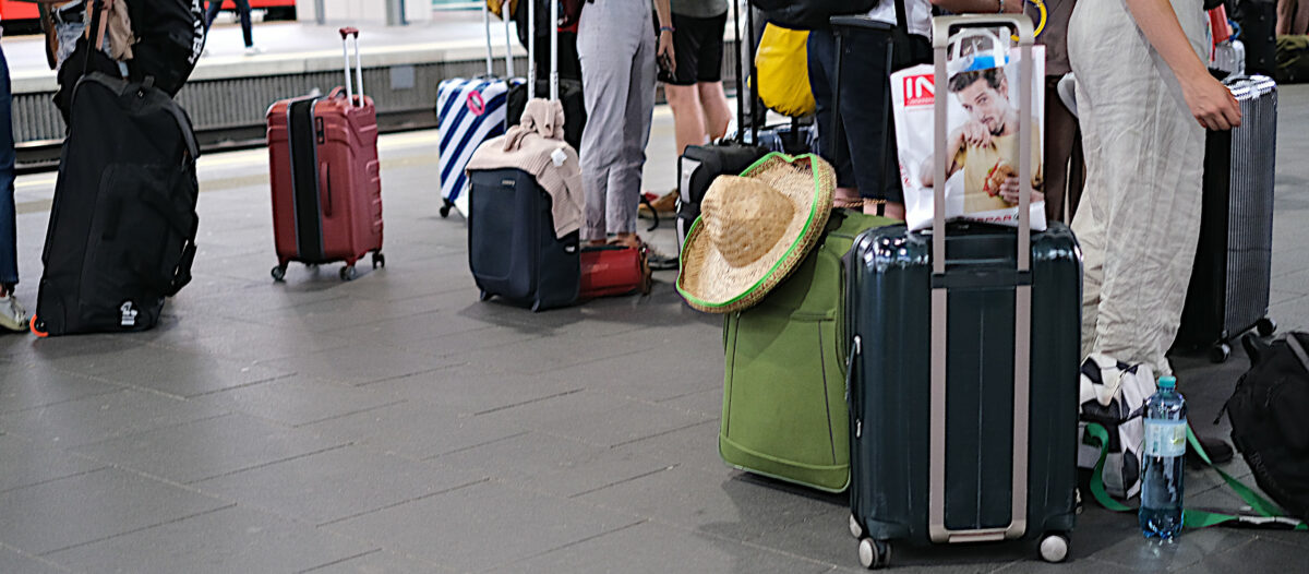 Various bags and suitcases in different forms and colors on the platform of Vienna main train station. A Panama hat indicates that it is summer vacation time.