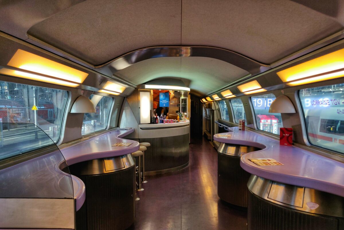 The interior of the TGV Duplex Bar area. It has puple standing tables on the sides next to the windows. It's a 1990ies design. At the end the bar. Nobody is there.